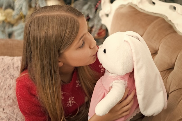 A kissable cutie Small girl kiss rabbit toy Little girl with cute bunny at Christmas tree Little child play with soft toy Small child happy smiling with present Best Christmas toy