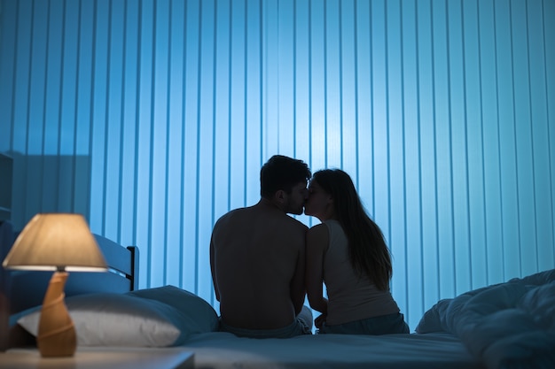 The kissing couple sit on the bed. night time