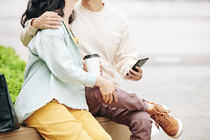 Photo スマートフォンでカップルにキスをし、公園のベンチに座ってコーヒーを取り出してキス