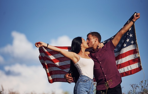 Kissing each other. Feels freedom. Beautiful couple with American Flag have a good time outdoors in the field.