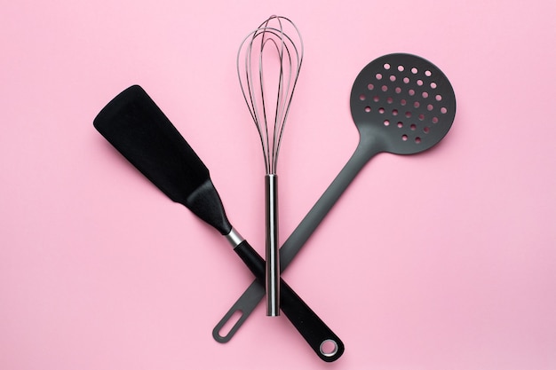 Kitchen accessories spatula whisk on a pink background