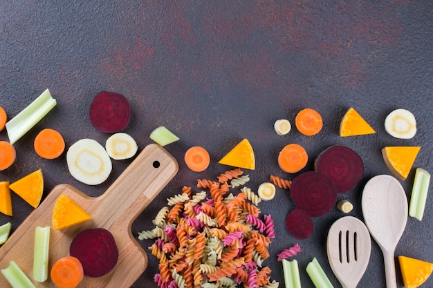 Kitchen background. Cooking delicious healthy food. Colorful dry pasta made from vegetables and its natural vegetable dyes celery, beet, carrot, pumpkin, parsnip.