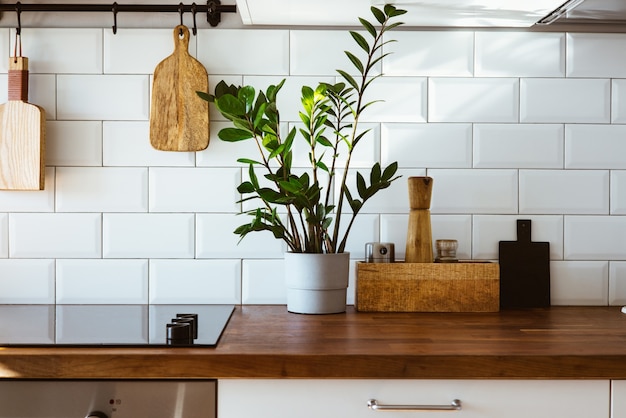 Kitchen brass utensils chef accessories hanging kitchen with white tiles wall and wood tabletopgreen plant on kitchen background early morning light