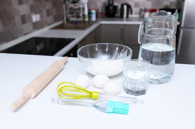 The kitchen counter has the ingredients for making homemade dough Flour eggs whisk rolling pin salt glass of water