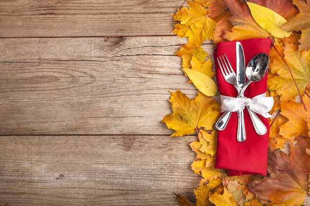 Kitchen cutlery on autumn leaves on wooden background