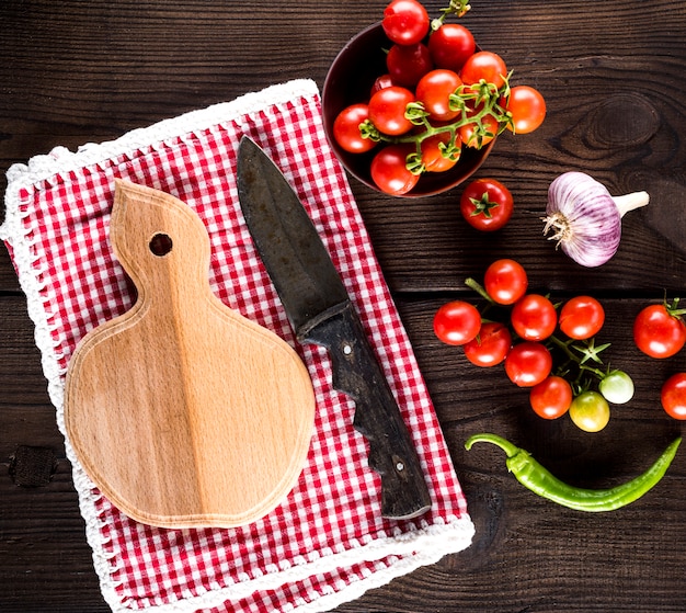 Kitchen cutting board and knife, near ripe red cherry tomatoes