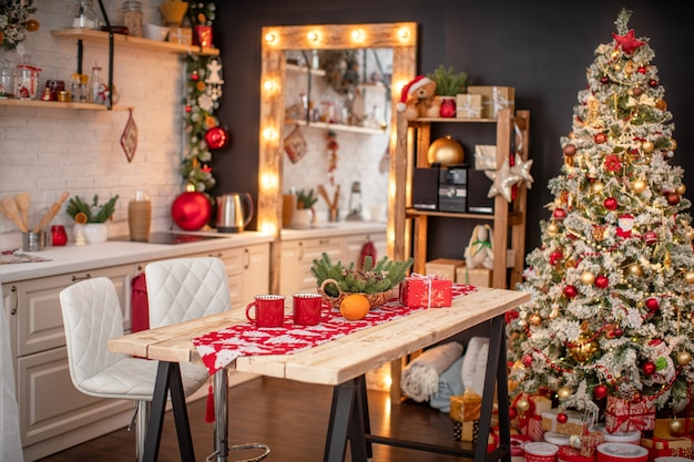 Kitchen decorated with pine garlands and Christmas toys. the table and near is worth Christmas tree. interior bright kitchen decorated for Merry Christmas and happy holidays!