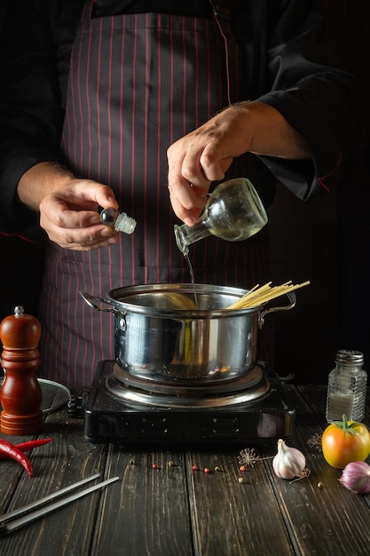 На кухне диетический суп готовится руками повара в горячей кастрюле Повар добавляет в еду растительное масло