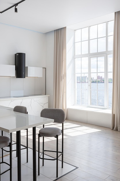 Kitchen and dining island with high bar stools in a minimalistic modern luxury design of an expensive house on a sunny day white walls with plaster parquet decorative lighting and no one inside