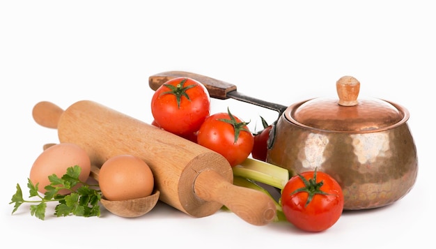 Kitchen equipment copper pan rolling pin spoons and different raw vegetables on a white background
