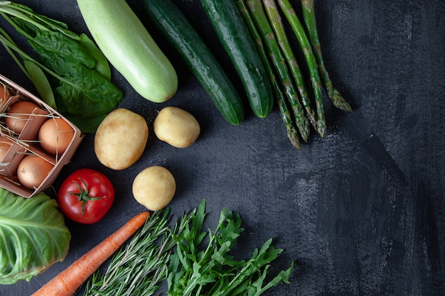 Cucina - organico fresco colorato, verdure di primavera su fondo di pietra scura. disposizione piana di carota, pomodoro, prezzemolo, asparagi e rosmarino. vista dall'alto cibo vegano. ingridients con spazio di copia. cocnept verde