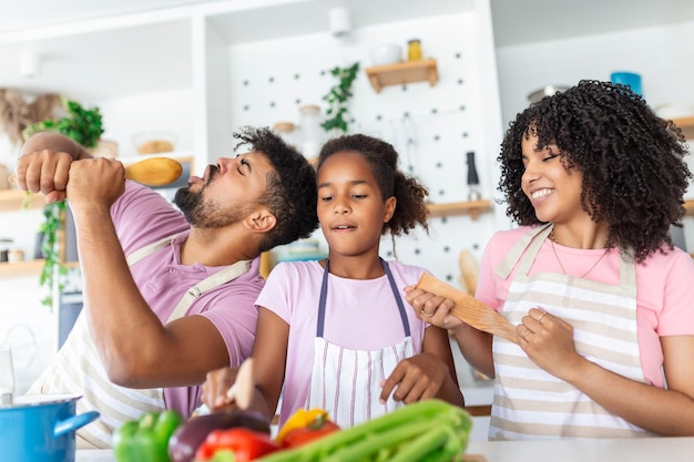 Kitchen Fun Cheerful parents and their little daughter singing while cooking together