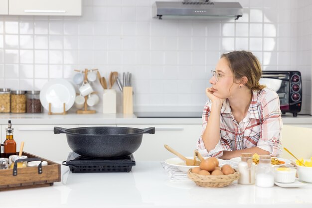 Nella cucina di casa, una bella donna con una tavoletta prepara un pasto a base di pasta e un'adorabile giovane donna mangia la pasta.