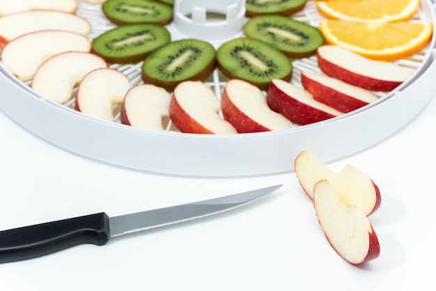 Kitchen knife and cut apple. Behind is a tray of dehydrator with slices of kiwi and apples.