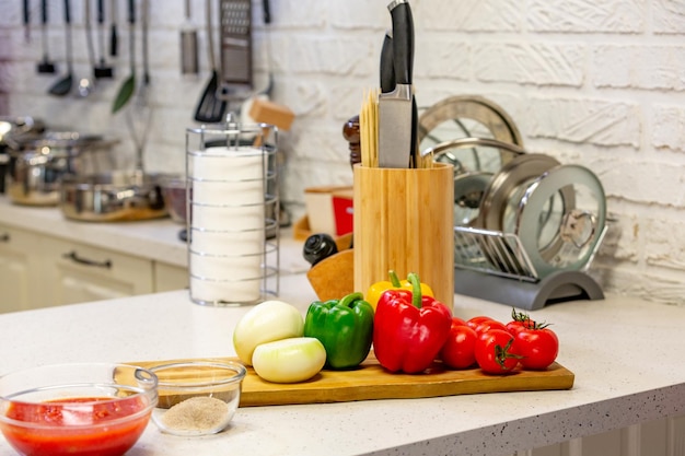 Kitchen knives in a special wooden stand with spice jars and fresh vegetables lie on a wooden board Closeup Kitchen concept