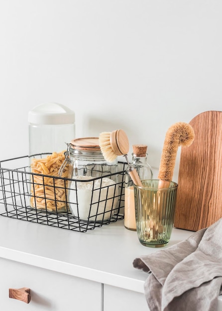 Kitchen organization interior cans of pasta flour in a metal basket brushes for washing dishes cutting boards napkin on a white table in a bright room