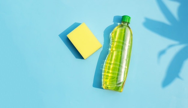 Kitchen sponge with bottle of dish washing liquid on blue surface