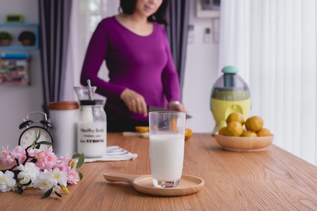 Tavolo da cucina con bicchiere di latte sulla donna che affetta il fondo di frutti.