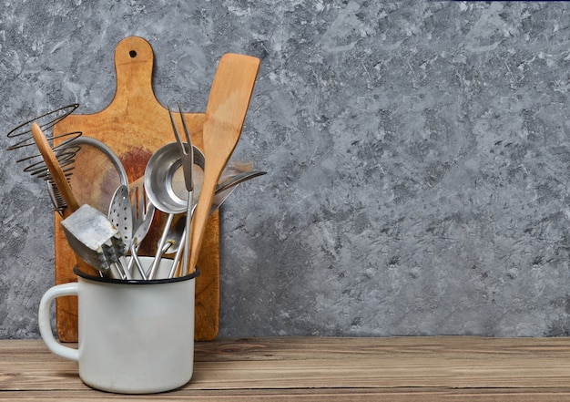 Kitchen tools for cooking on a wooden table on the background of a concrete wall.Copy space. Spoons, forks, wooden spatula.