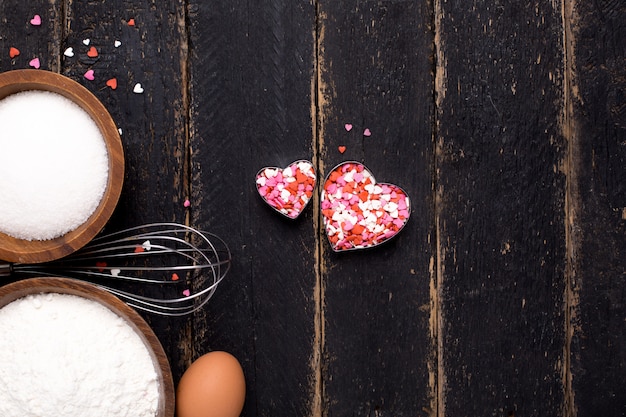 Kitchen tools, flour, hearts and sugar on wood