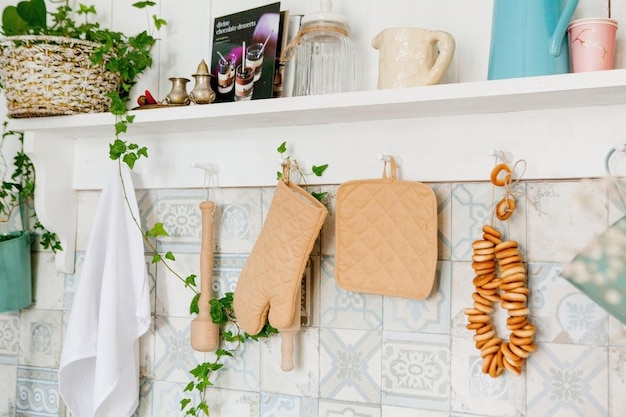 Кухонное полотенце и перчатка на столешнице в современной кухне Кухонные принадлежности висят на рейлинге на белой стене