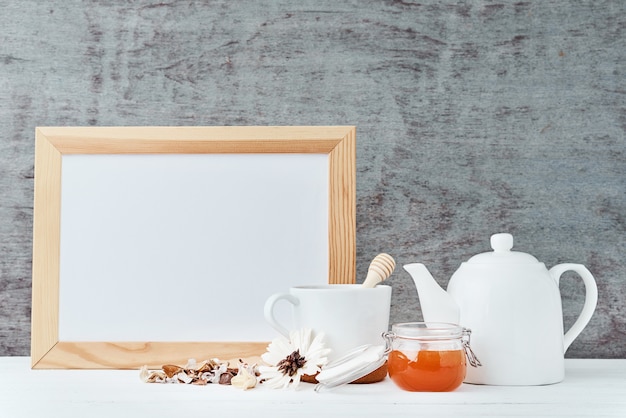 Fondo degli utensili della cucina con libro bianco vuoto, teiera, tazza e un miele in barattolo di vetro