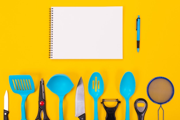 Kitchen utensils and clean sheet of paper isolated on yellow background