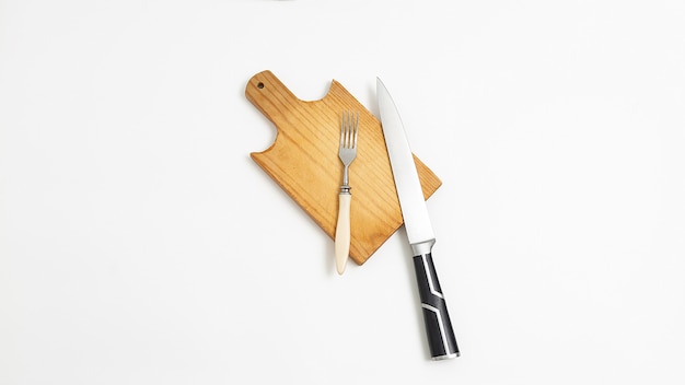 Kitchen utensils: knife with metal blade, black handle and fork on cutting board