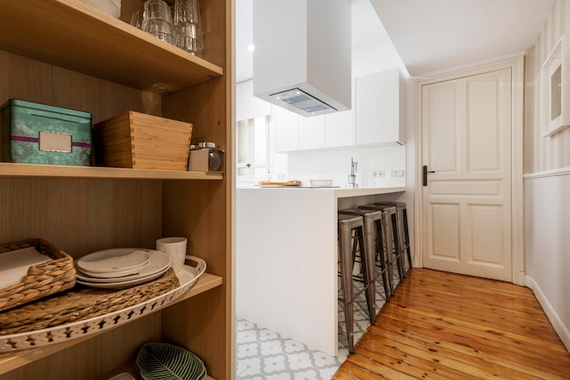 Kitchen with large plain white onepiece cabinet and stainless steel appliances with wooden floors and hydraulic stoneware and pantry with accessories at the entrance