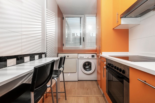 バケーション レンタル アパートメントのオレンジ色のキャビネット ホワイト カウンター トップと白い電化製品を備えたキッチン