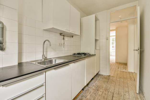 A kitchen with white cabinets and black counter tops on the floor in front of an open door that leads to another room