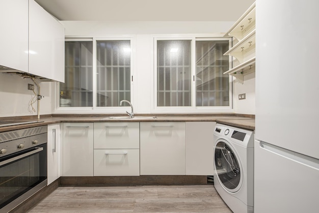 Kitchen with white cabinets brownstone worktops twin barred windows and a white washing machine and fridge