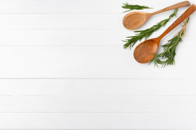 Cucchiaio da cucina in legno con rosmarino su fondo di legno bianco