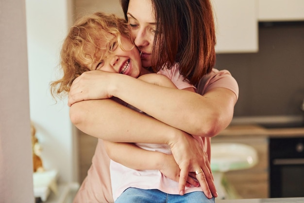 Photo on the kitchen young mother with her little daughter in casual clothes together indoors at home