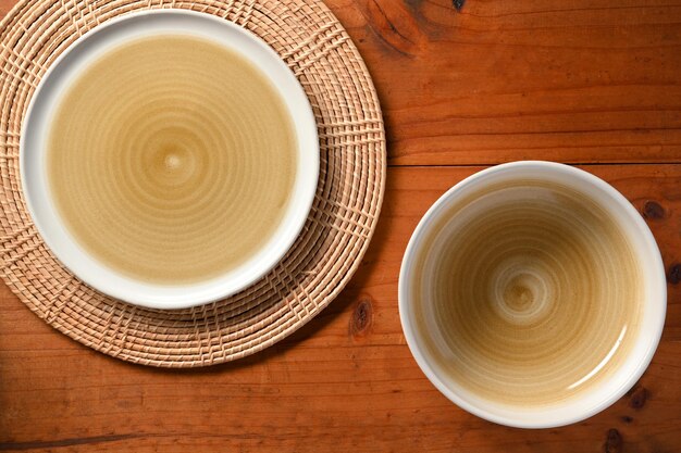 Kitchenware Empty minimalist ceramic plate on bamboo placemat and bowl on wooden background above