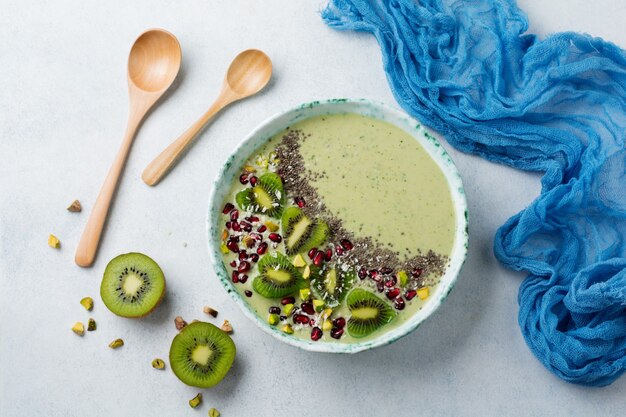 Kiwi banana smoothies bowl with oatmeal, pistachio nuts, pomegranate seeds and chia on light gray stone background