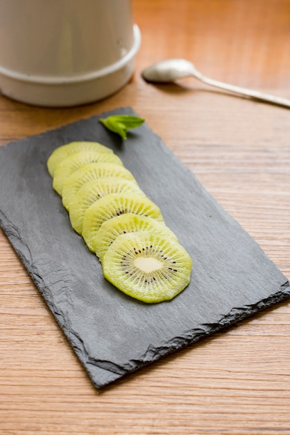 Kiwi on blackboard with mint next to spoon and teapot on wooden background