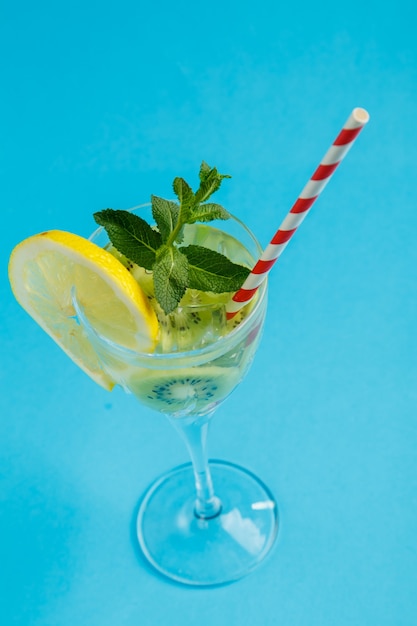 Kiwi cocktail garnished with lemon and mint in a glass on a napkin against a blue surface