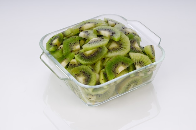 Kiwi fruit slices or cut piece arranged in a glass square container with white color background.