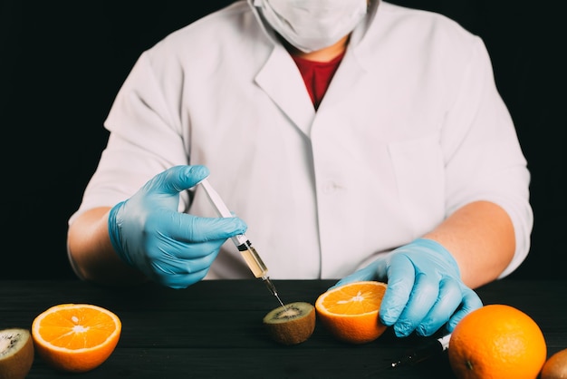 Kiwi injections lab technician in bathrobe and gloves colitis nitrates and gmo in kiwi on black background in the studio