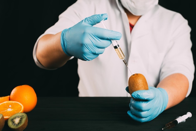 Kiwi injections lab technician in Bathrobe and gloves colitis nitrates and GMO in Kiwi on black background