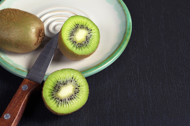 Kiwi e coltello nel piatto sul tavolo di pietra nera