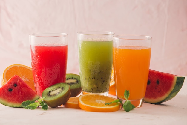 kiwi, orange and watermelon smoothie and various pieces of fruit over wooden background