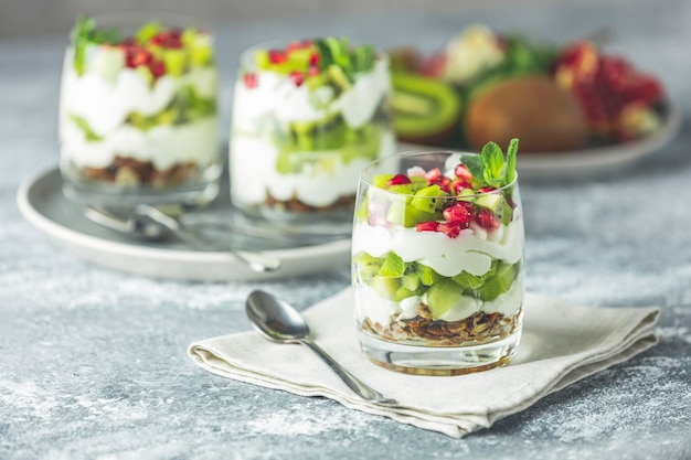 Kiwi parfait dessert in glass with ingredients Yogurt granola and fruits Healthy snack or breakfast Light gray concrete surface