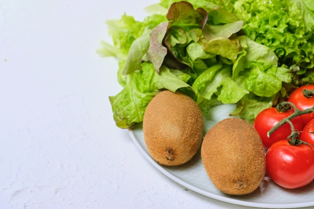 Kiwi's, sla en cherry tomaten op een witte plaat op een witte achtergrond