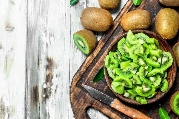 Photo kiwi slices in a bowl on a cutting board with a knife