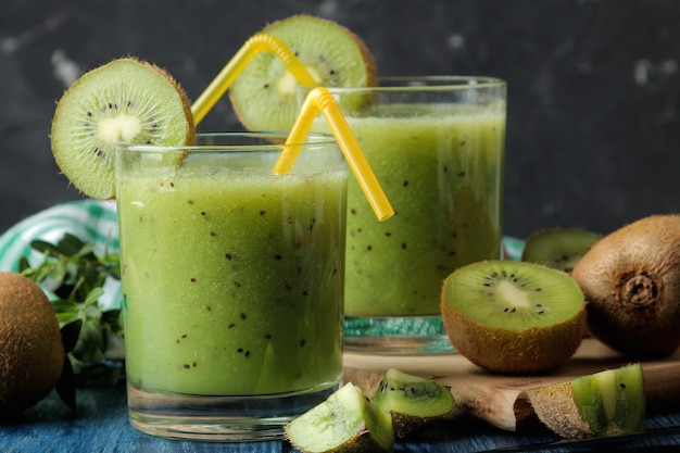 Kiwi smoothies in a glass next to fresh kiwi slices on a blue wooden table. fruit drink.