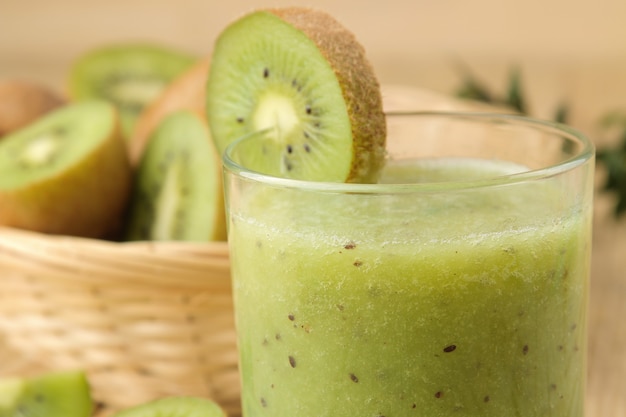 Kiwi smoothies in a glass next to fresh kiwi slices on a natural wooden table.