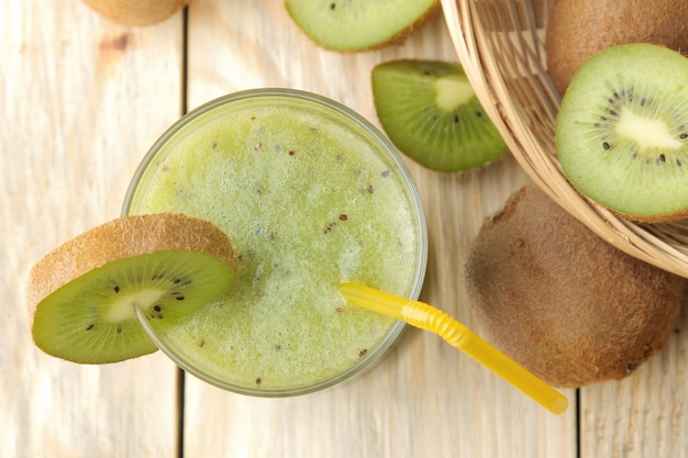 Kiwi-smoothies in een glas naast verse kiwiplakken op een natuurlijke houten tafel. bovenaanzicht