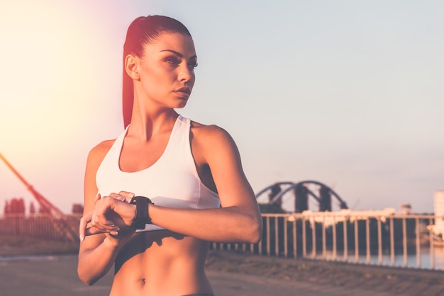 Klaar om nu te rennen. Mooie jonge vrouw in sportkleding die smartwatch draagt en wegkijkt